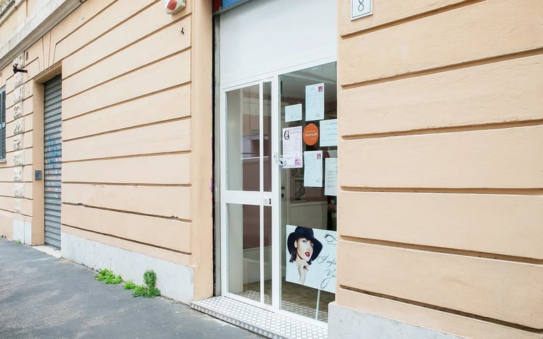 Modern storefront entrance with glass door and beige horizontal siding, notices posted on glass, sidewalk with small plants