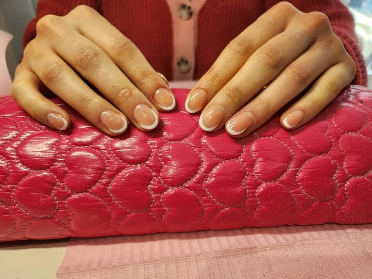 Person displaying manicured nails with nude polish on red quilted clutch