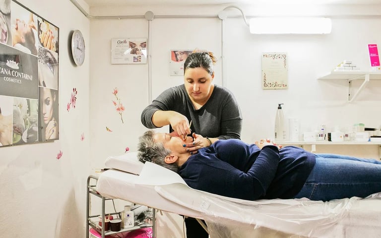 Therapist performing facial massage on elderly client lying on treatment table in clinic room