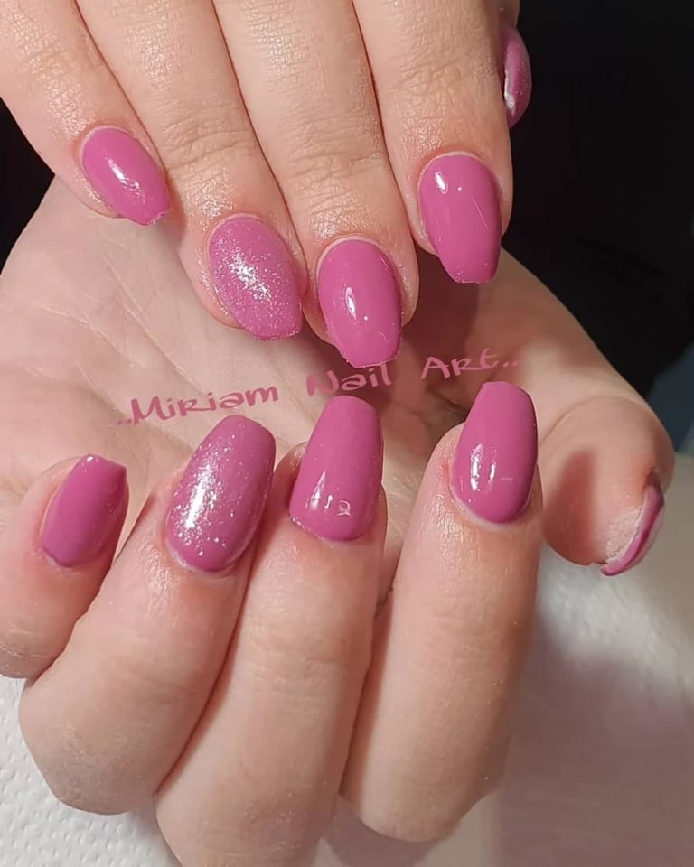 Close-up of manicured nails with pink polish and glittery accents on some nails, displayed on a white surface