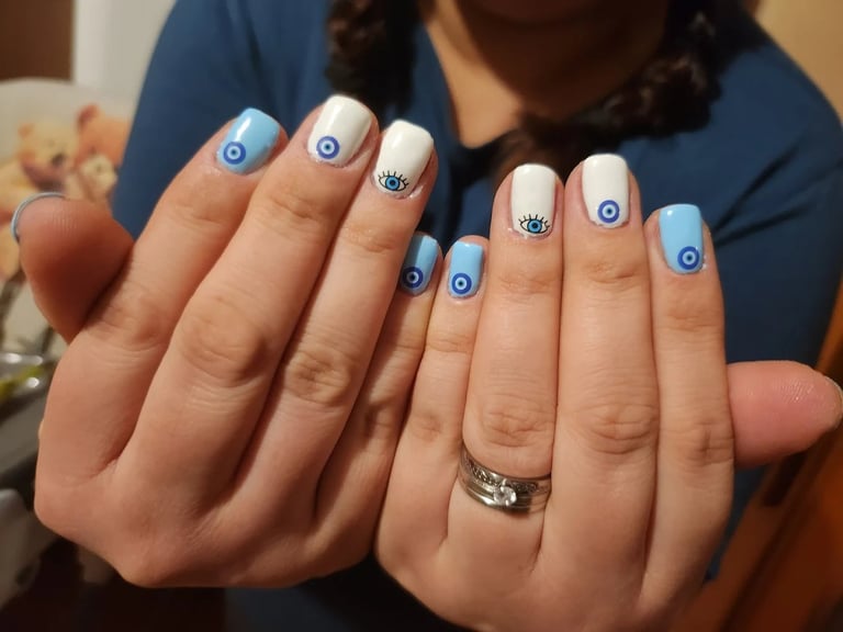 Person displaying manicured nails with blue and white nail art featuring evil eye designs